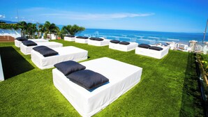 Outdoor lounge chairs on a grassy area with a view of the ocean and city skyline. - Soho PV: Luxury, Art, and Breathtaking Views (Puerto Vallarta)
