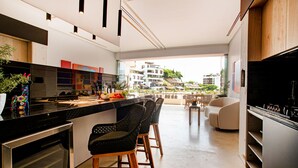 A modern kitchen with a central island, bar stools, a dining area with a sofa, and a view of buildings in the background. - Soho PV: Luxury, Art, and Breathtaking Views (Puerto Vallarta)