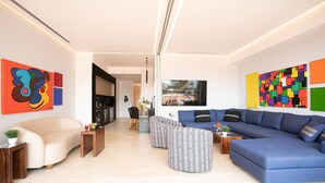 A modern living room with a sofa, ottoman, and a dining area with a table and chairs. - Soho PV: Luxury, Art, and Breathtaking Views (Puerto Vallarta)