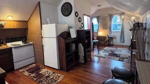 A compact kitchen with a stove, refrigerator, and wooden flooring. There is a dining area with a table and chairs, and a living space with a sofa and a rug. - The Ember Loft (Everett)