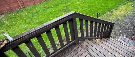 A wooden deck with a metal railing, a grassy yard, and a wooden fence.