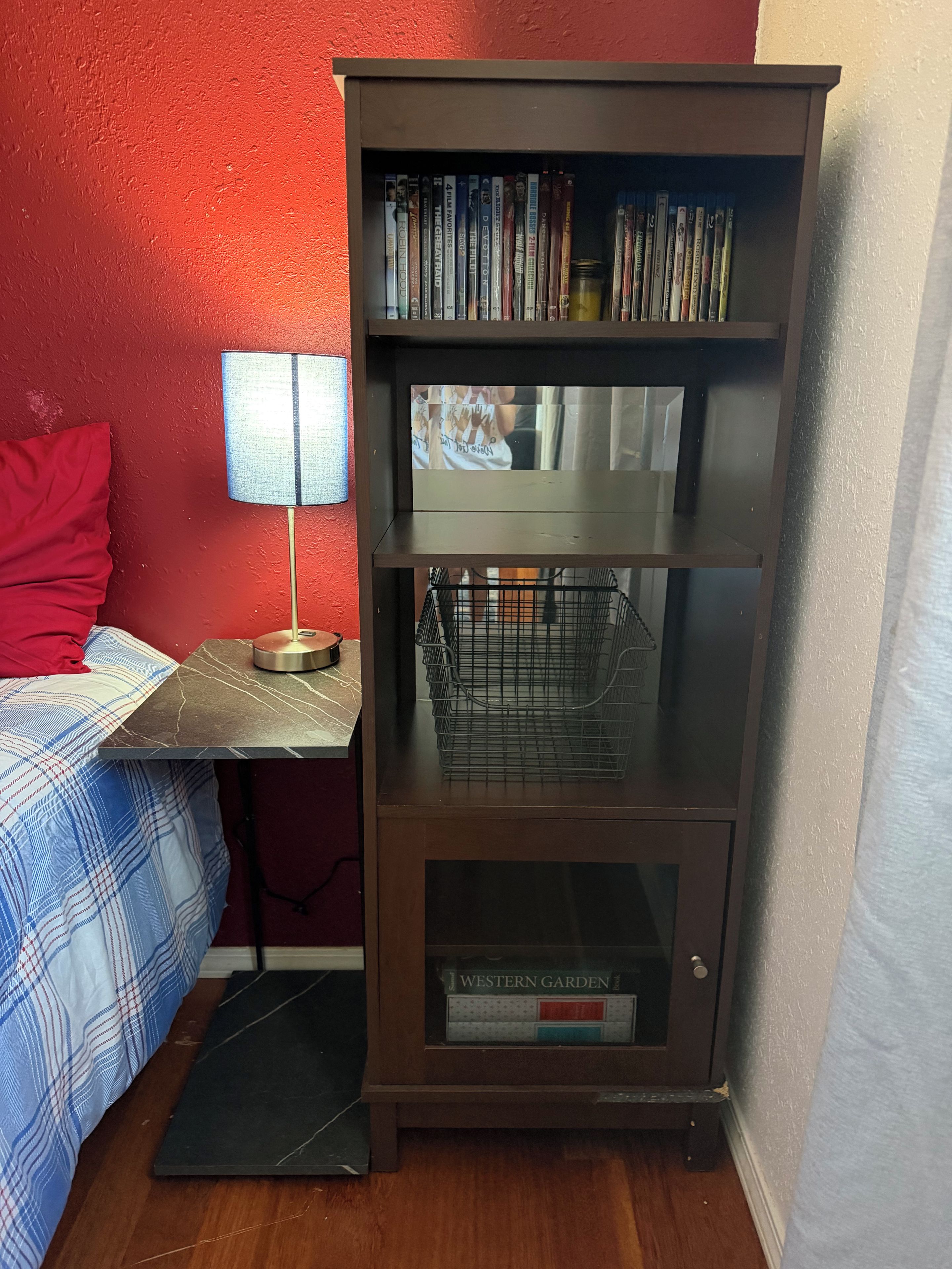 A room with a bed, a lamp, a bookshelf, and a scale.