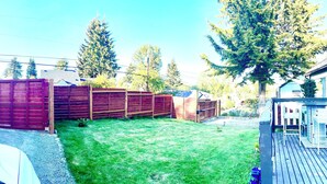A fenced backyard with a grassy lawn, a wooden deck, and a house in the background. - The Ember Loft (Everett)