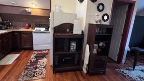 A compact kitchen with a stove, sink, and white cabinets. There is a wooden floor and a rug in the living area. - The Ember Loft (Everett)