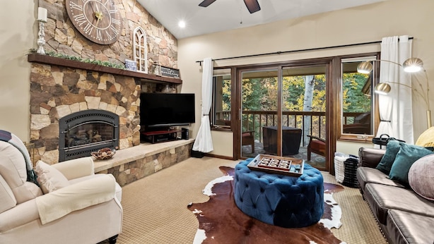 A living room with a stone fireplace, a large clock, and a ceiling fan. - Winterwood 11 – Cozy 3BR Mountain Townhome with Sauna and Creek Views! (Steamboat Springs)