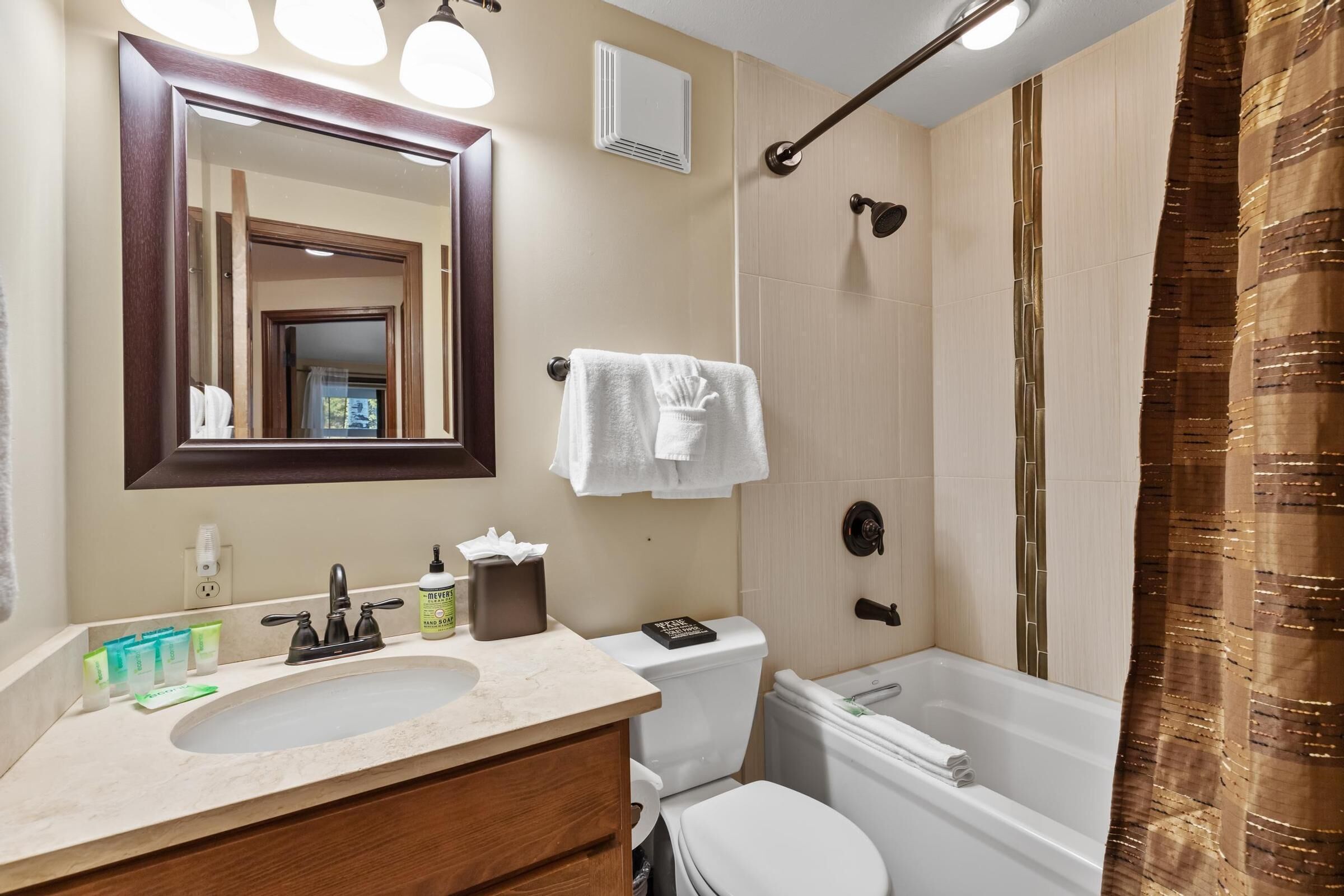 A bathroom with a sink, mirror, toilet, and bathtub.