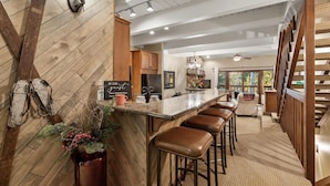 A modern kitchen with wooden accents, a bar area with stools, and a view of the outdoors. - Winterwood 11 – Cozy 3BR Mountain Townhome with Sauna and Creek Views! (Steamboat Springs)