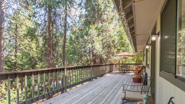 A wooden deck with outdoor furniture, a red umbrella, and a frog statue. - Huckleberry House- Rec Room (Arnold)