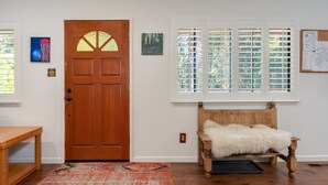 A room with a wooden door, a bench with a fur throw, a patterned rug, and a window with blinds. - Huckleberry House- Rec Room (Arnold)