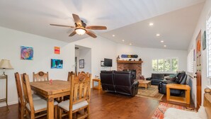 A spacious living room with a dining area, wooden furniture, a fireplace, and a ceiling fan. - Huckleberry House- Rec Room (Arnold)