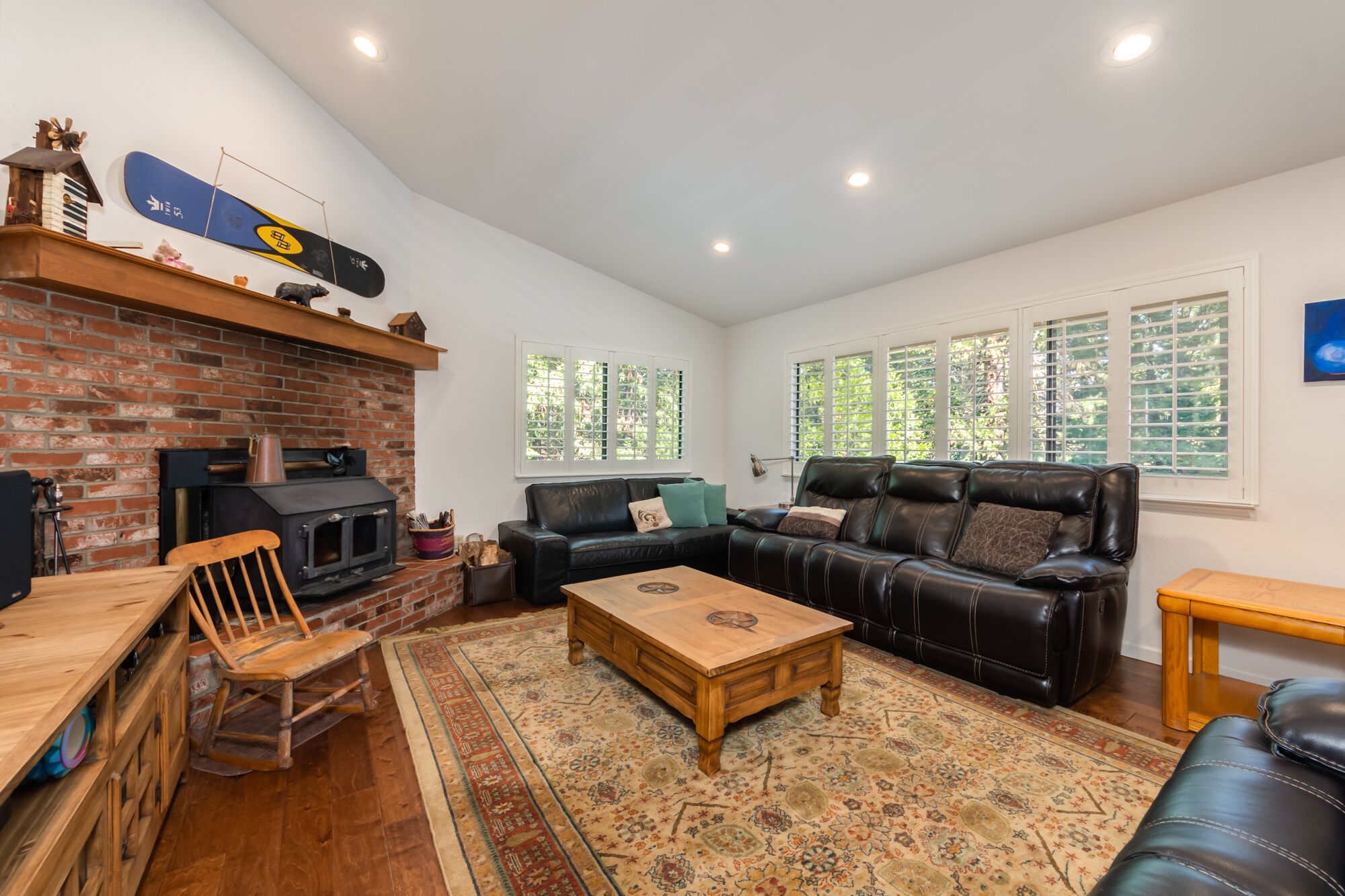 A cozy living room with a brick fireplace, a leather sofa, a wooden coffee table, and a patterned rug.