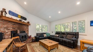 A cozy living room with a brick fireplace, a leather sofa, a wooden coffee table, and a patterned rug. - Huckleberry House- Rec Room (Arnold)