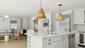 Una cocina moderna con armarios blancos, una isla central y dos lámparas colgantes de mimbre.