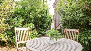 A round wooden table with two chairs, surrounded by lush greenery and a stone wall. - Higher Norton Barn (Totnes)