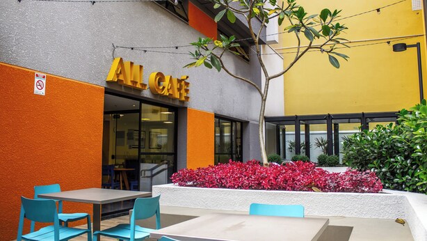 An outdoor seating area with tables and chairs, a building with a yellow and orange facade, and a sign that reads "ALCafé". - Complete studio in the center of Curitiba. (Centro Curitiba)