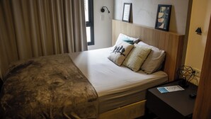 A neatly made bed with a blanket, pillows, and a bedside table with a remote control and a framed picture. - Complete studio in the center of Curitiba. (Centro Curitiba)