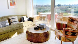 A living room with a sofa, a round coffee table, and a patterned armchair. There is a large window with a view of greenery and a white ceiling. - Penthouse with the green kitchen and view of Brijuni in Peroj (Peroj)