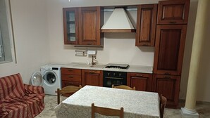 Una cucina compatta con mobili in legno, una lavatrice integrata e un'area pranzo con tavolo e sedie.