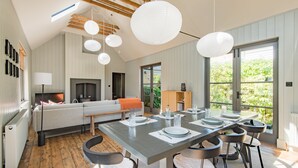 Un salon moderne doté d’une cheminée, d’une table à manger dressée pour six personnes et d’une grande fenêtre offrant une vue sur la verdure.