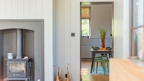 Un intérieur chaleureux avec un poêle à bois, un coin repas avec des chaises et une fenêtre équipée de stores.