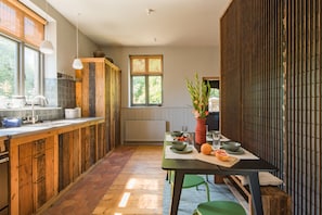 Une cuisine avec des meubles en bois, une table à manger dressée pour deux personnes et une fenêtre donnant sur un paysage verdoyant.