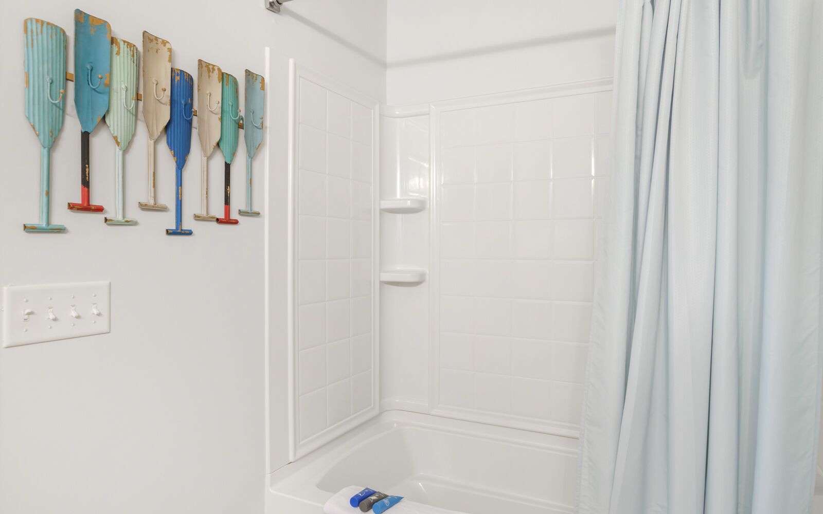 A shower area with a white tiled wall, a white shower curtain, and a set of colorful, vintage-looking shower sponges hanging on the wall.