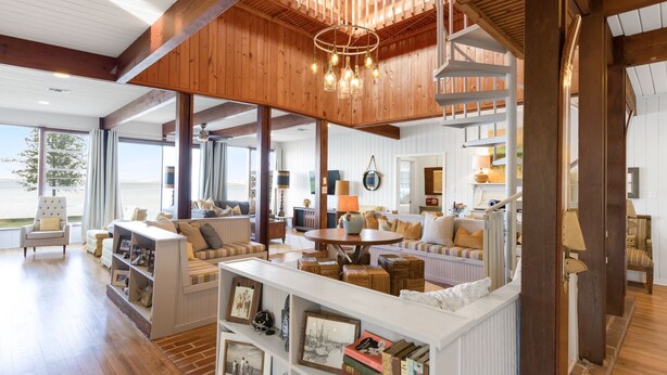 Een ruime woonkamer met houten balken, een groot raam met uitzicht op een wateroppervlak en een gezellige zithoek.
