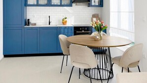 A modern kitchen with blue cabinets, a white tiled backsplash, a round wooden table, and a pendant light. - Penthouse with the blue kitchen and view of Brijuni in Peroj (Peroj)