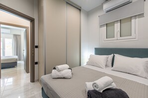 A modern hotel room with a large bed, a separate seating area, and a view of the hallway. - Neaira city apartment near the beach (Chania)