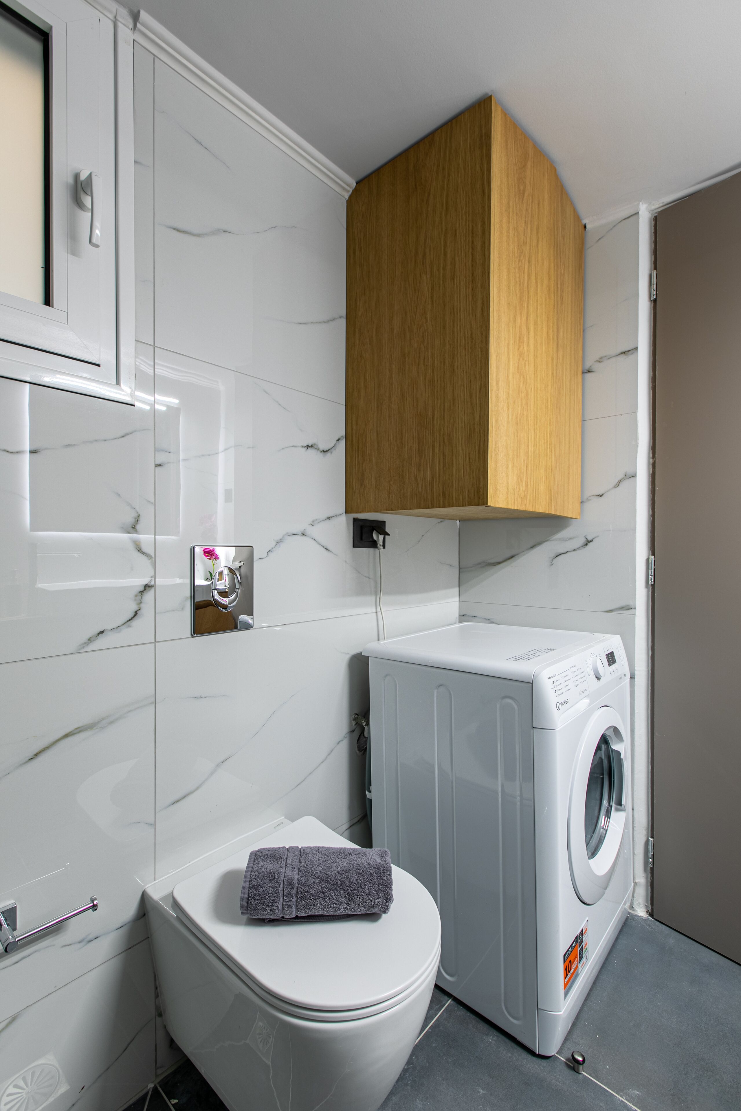 Ein kleines Badezimmer mit Toilette, Waschmaschine und einem Holzschrank darüber.