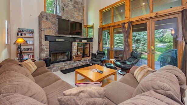 A cozy living room with a stone fireplace, leather furniture, and large windows offering a view of the outdoors. - Family Ski Retreat w/ Hot Tub & Views (McHenry)
