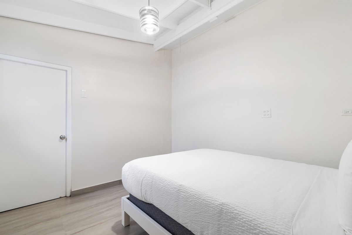A bedroom with a bed, a door, and a ceiling light fixture.