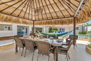 An outdoor dining area with wicker furniture, a thatched roof, and a hammock.