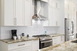 A kitchen with white cabinets, a stainless steel range hood, a gas stove, a built-in oven, and a refrigerator.