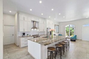 A modern kitchen with white cabinetry, a marble island with bar stools, and a large window providing natural light.