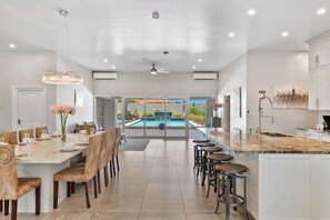 A spacious kitchen with a large island, a dining area with wicker chairs, and a view of a swimming pool.