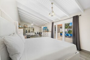 A bedroom with a large bed, a desk with a chair, a television, and a view of a pool area. - Luxurious 7BR Villa w/ Private Pool & Palapa (Noord)