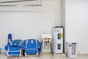 Ein Zimmer mit weißer Wand, einem Durchlauferhitzer, einem Wäschekorb und mehreren blauen Stühlen.