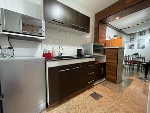 Una cocina con armarios oscuros, microondas, hervidor y cafetera.