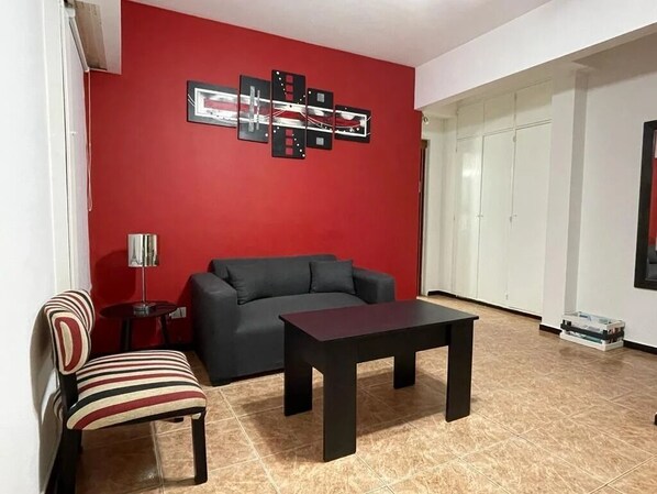 Una sala de estar con una pared roja, un sofá negro, una silla a rayas y una mesa de madera oscura.