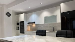 A modern kitchen with white cabinets, a marble countertop, and black chairs. - Appartement de Luxe Avec vue sur mer à Malabata (Tanger)