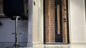 A modern interior with a sleek, dark-colored chair, a polished floor, and a wooden door with a black frame. - Appartement de Luxe Avec vue sur mer à Malabata (Tanger)