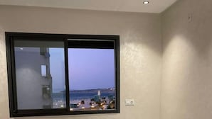 A bedroom with a large window, a bed, and a view of a cityscape. - Appartement de Luxe Avec vue sur mer à Malabata (Tanger)