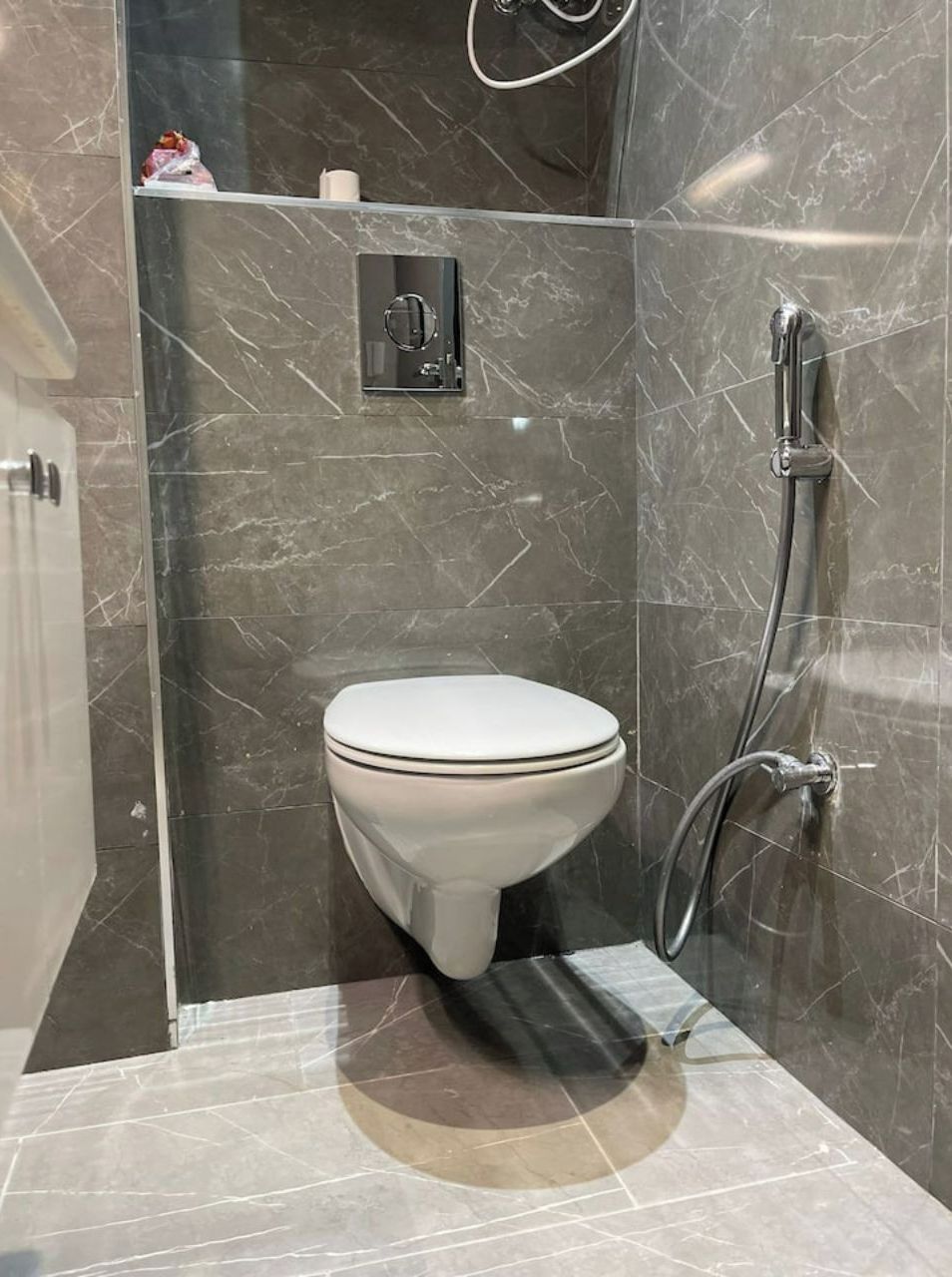A modern bathroom with a white toilet, a glass-enclosed shower area, and a marble-tiled floor.