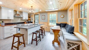 A spacious kitchen with wooden cabinets, a central island with stools, and a dining area with a bench and table. - Dock & Beach Access! Waterfront Home on Kezar Lake (Lovell)