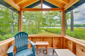 A wooden cabin with a large window offering a view of a forest and lake. - Dock & Beach Access! Waterfront Home on Kezar Lake (Lovell)