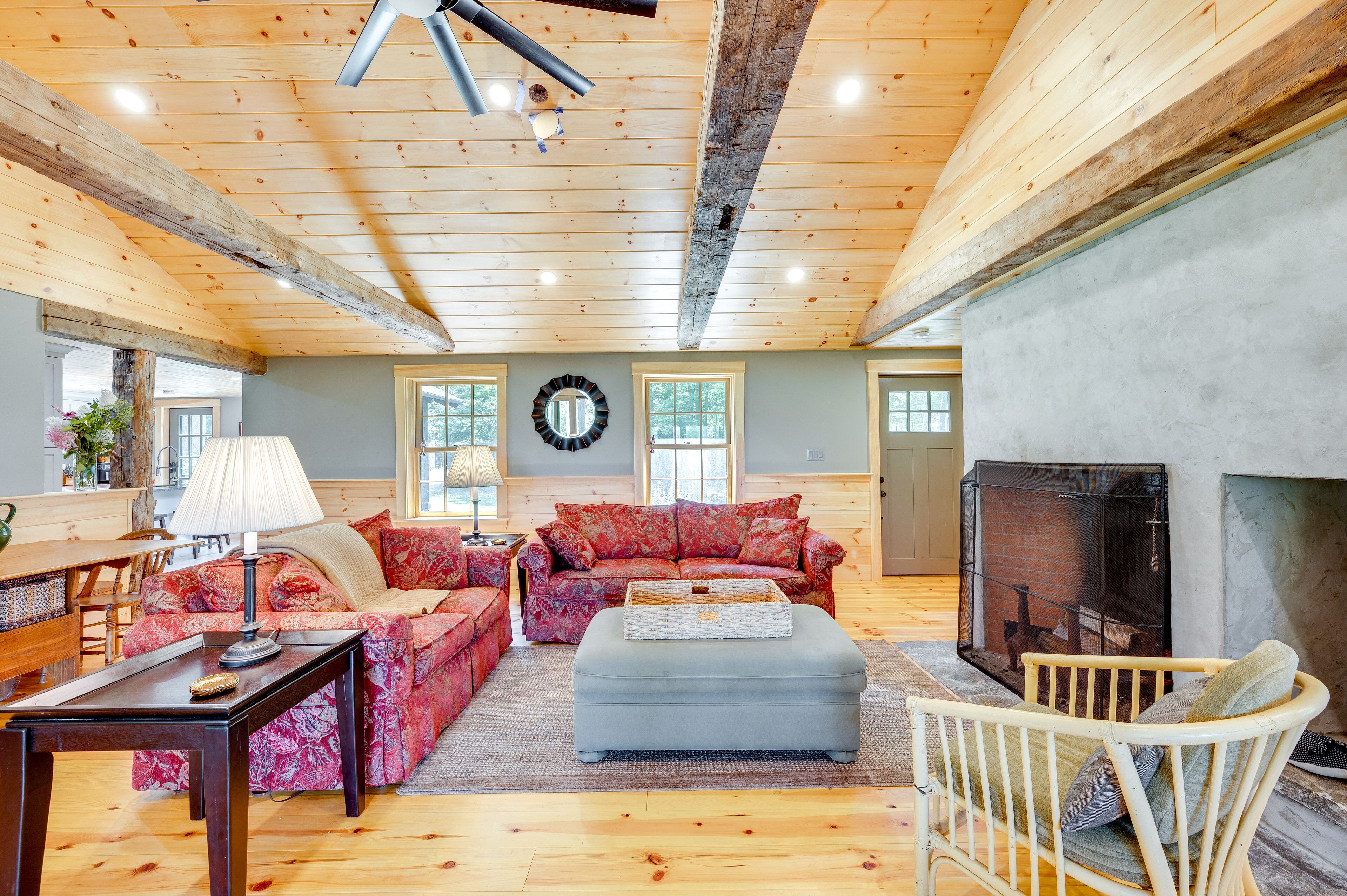 A cozy living room with wooden beams, a fireplace, and a large window.