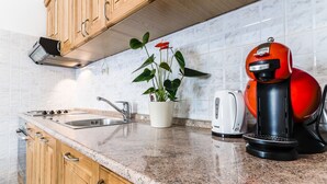 A kitchen with wooden cabinets, a granite countertop, a sink, a kettle, a coffee maker, and a potted plant. - A cozy apartment, 1 km from the beach in a quiet neighborhood (Vrsar)