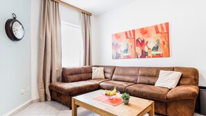 A living room with a brown leather sofa, a wooden coffee table with a bowl of fruit and a plant, a clock on the wall, and a large abstract painting. - A cozy apartment, 1 km from the beach in a quiet neighborhood (Vrsar)