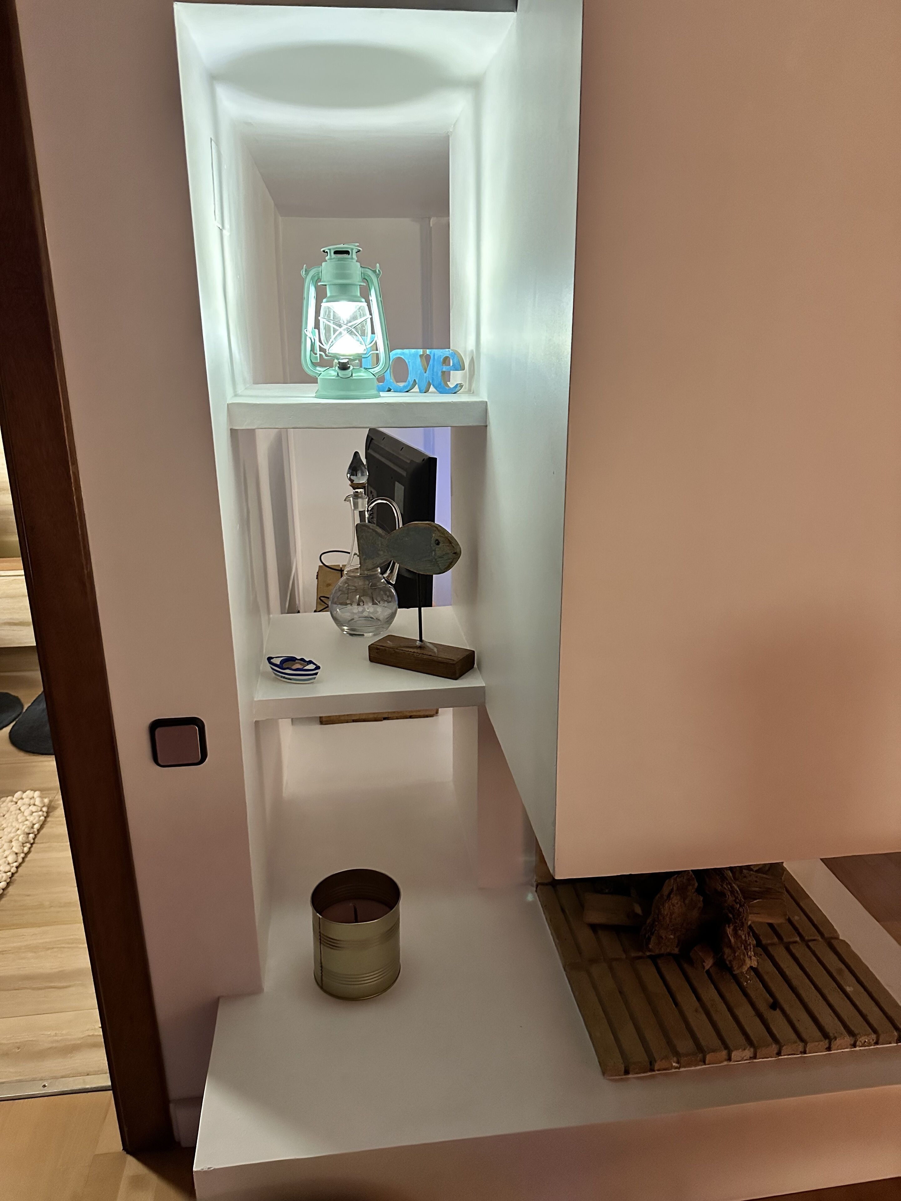 Une étagère blanche ornée d’objets décoratifs, notamment un flacon en verre, une sculpture en métal et un petit bol.